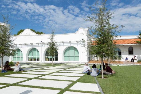 A group of people sitting on a lawn in front of a white building.