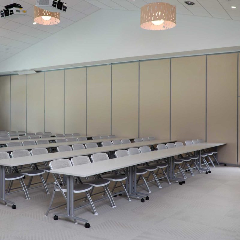 Picture of the Multipurpose Room side 1. Shows folding chairs, tables, window, and exit door to the outside.