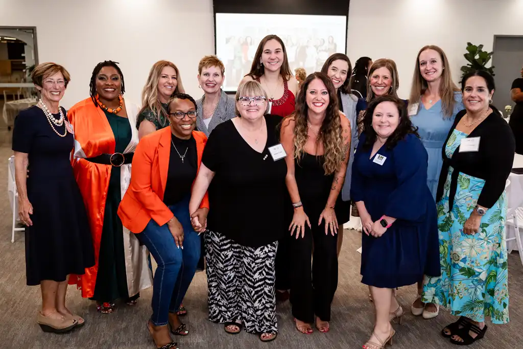 A diverse group of women standing together in a conference room, smiling for a group photo.