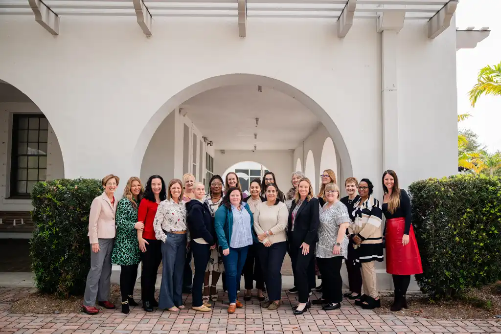 A diverse group of adults standing in a line outdoors in front of a white arched building, posing and smiling.