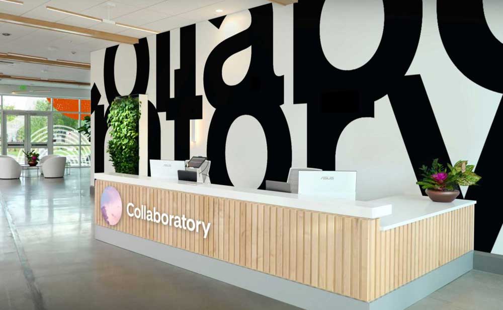 Bright, modern collaboratory reception with a wood-paneled front desk and bold black typography on the wall.